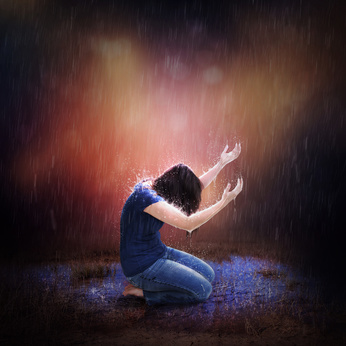 A woman kneeling to pray during a heavy rain storm.